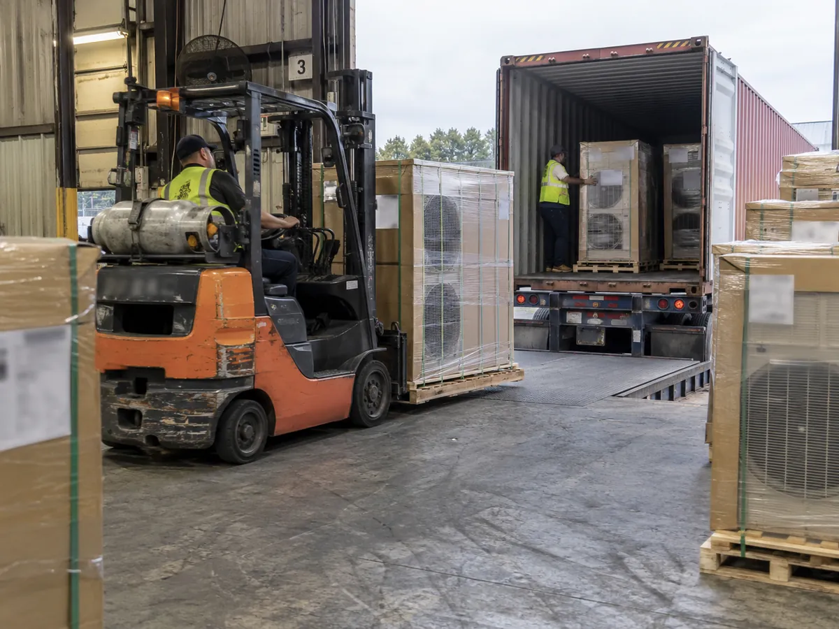Industrial loading dock with generic HVAC outdoor units being moved toward a shipping container.